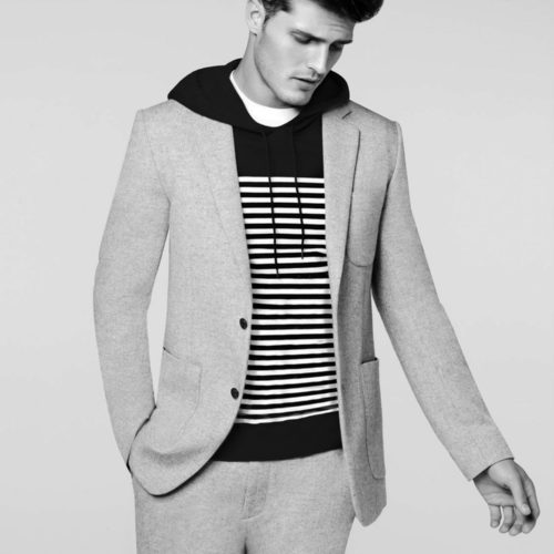 Black-and-white image of a male model in a light grey tweed suit over a black hoodie with white stripes, for Details.