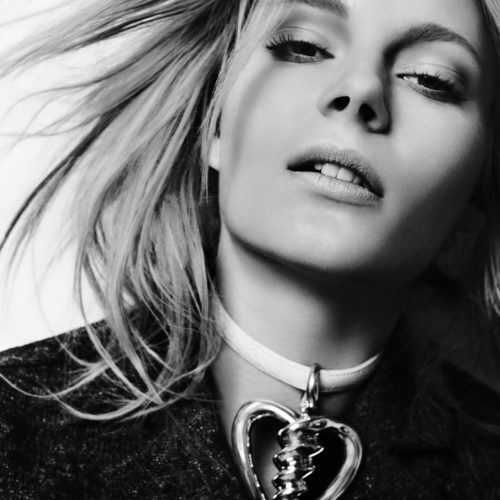 Black and white close-up of a blonde model with windswept hair wearing a choker with a heart pendant, for French Revue des Modes.