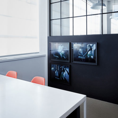 Office interior with white table, orange chairs and three framed blue-toned photographs on a dark wall, for Giovanni Bianco.