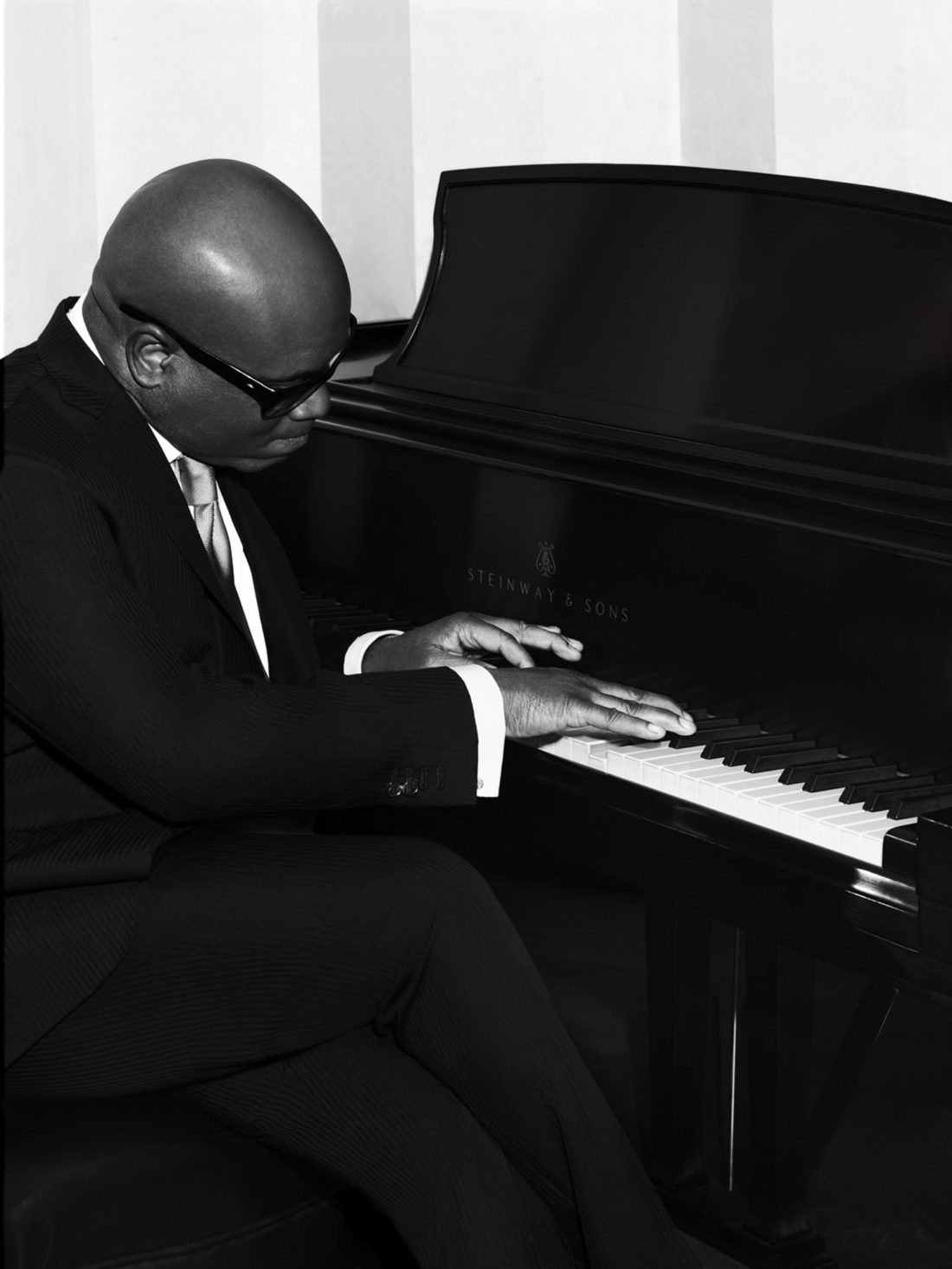 Black-and-white portrait of L.A. Reid in a pinstripe suit and sunglasses playing a Steinway grand piano.