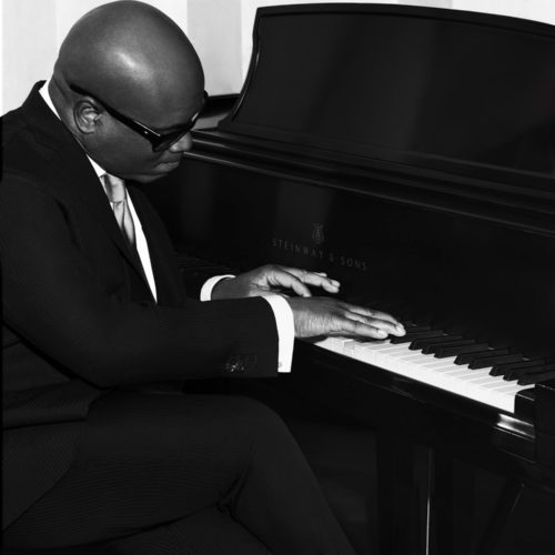 Black-and-white portrait of L.A. Reid in a pinstripe suit and sunglasses playing a Steinway grand piano.