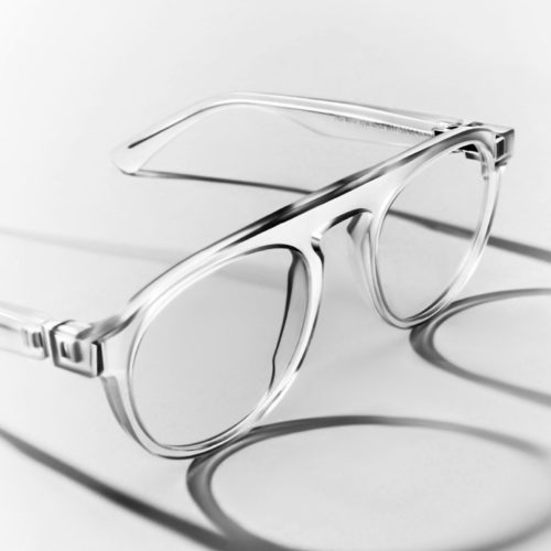 Clear acetate eyeglasses with metal hinges casting long shadows on a white surface, in black and white, for Maison Margiela.