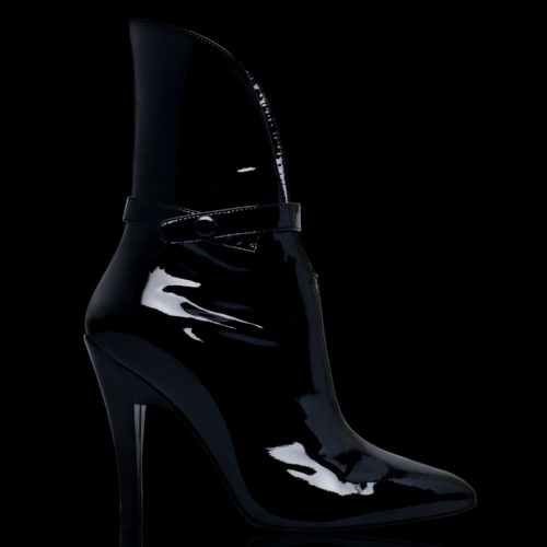 Black patent leather stiletto ankle boot with button strap, lit against a black background, for Mechante of London.