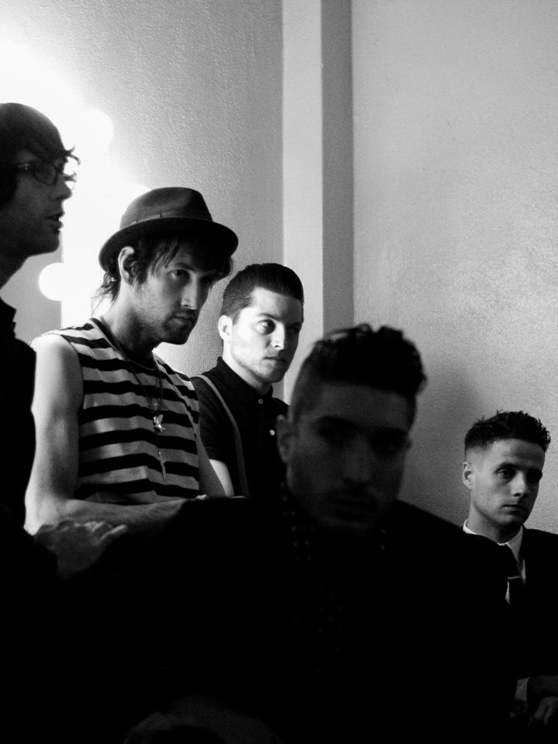 Black and white portrait of the five members of The Bravery gathered backstage beside a lit dressing-room mirror.