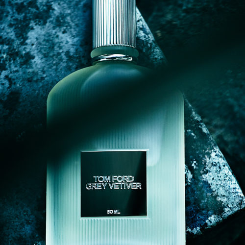 Frosted Grey Vetiver fragrance bottle with ribbed silver cap lying on dark blue-green stone, for Tom Ford.