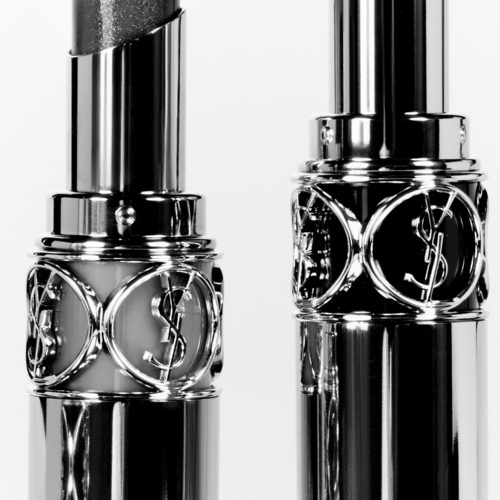 Two open lipsticks in chrome cases with cutout YSL monograms, shot close up in black and white, for YSL.