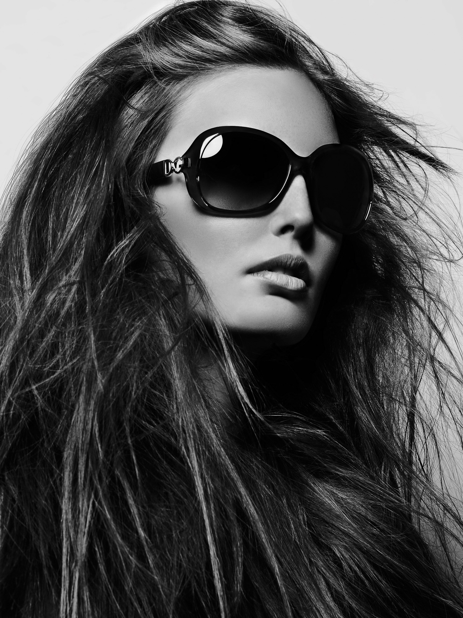 Black and white close-up of a model with long windswept hair wearing oversized black D&G sunglasses, for Vogue China.
