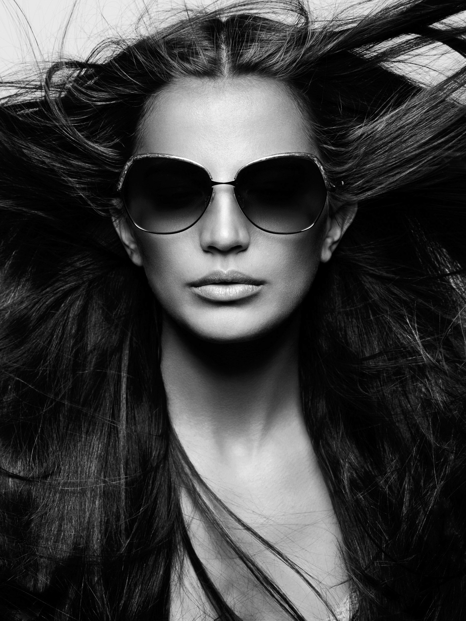 Black and white portrait of a model with windswept long dark hair wearing oversized sunglasses, for Vogue Italia.