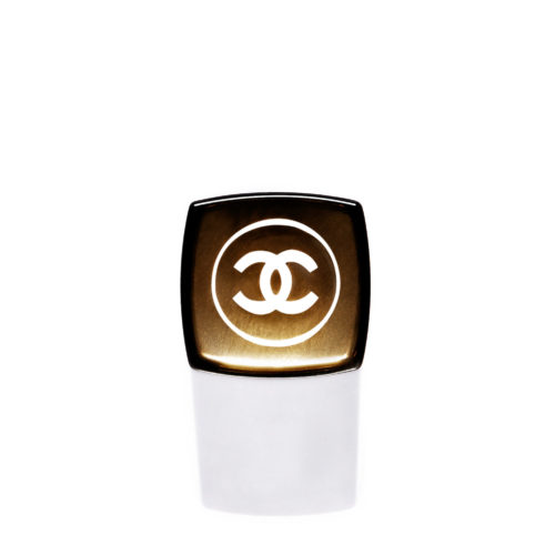 Black and gold lipstick cap with the interlocking CC emblem on a white background, for Chanel.