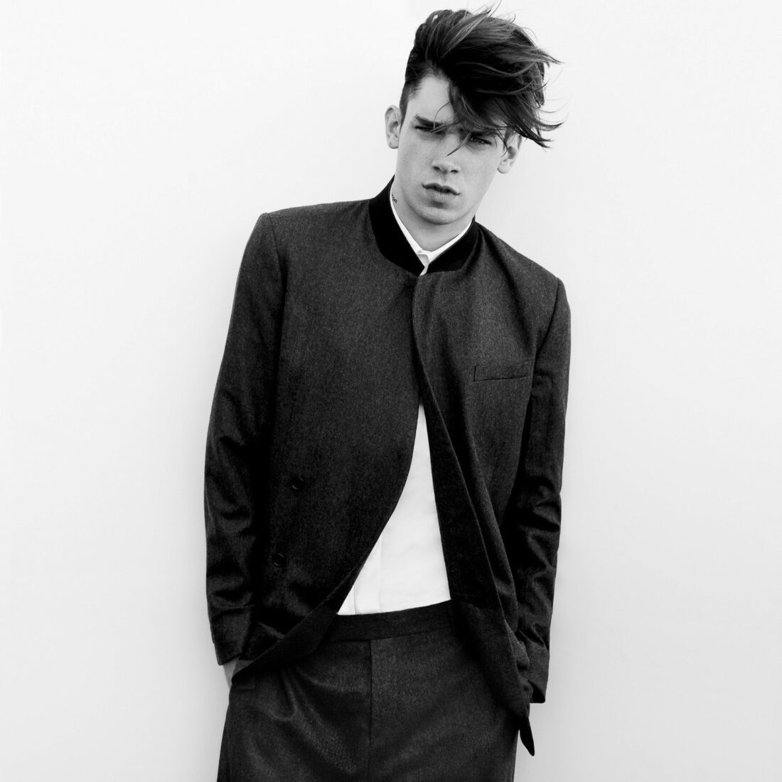 Black and white shot of a young male model with swept hair in a dark collarless jacket and white shirt, for Dazed & Confused.