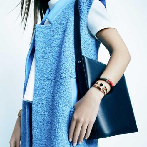 Model in a blue shearling vest and white top with a navy leather shoulder bag and gold bangles, for InStyle.