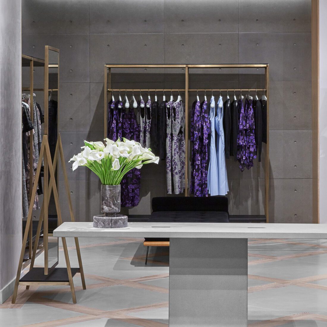 Boutique interior with purple floral dresses on a brass rack, concrete walls and white calla lilies on a table, for Jason Wu.