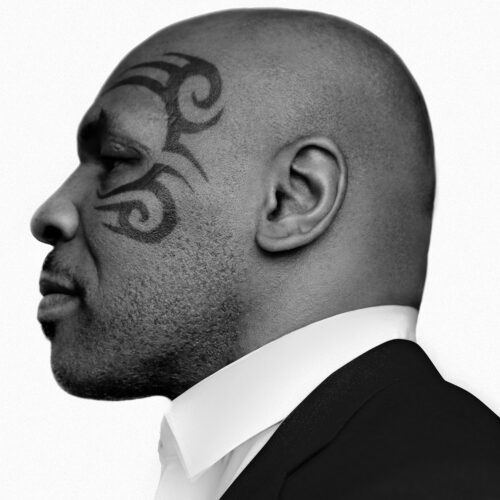 Black and white profile portrait of Mike Tyson with his tribal face tattoo, wearing a white shirt and dark suit.