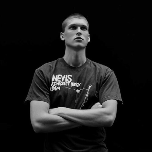 Black and white portrait of a young man with a buzz cut, arms crossed, wearing an AJ Hackett Nevis Bungy T-shirt.
