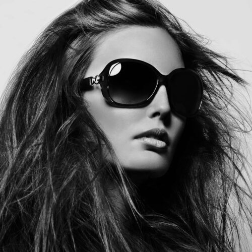 Black-and-white close-up of a model with windswept long hair wearing oversized D&G sunglasses, for Vogue China.