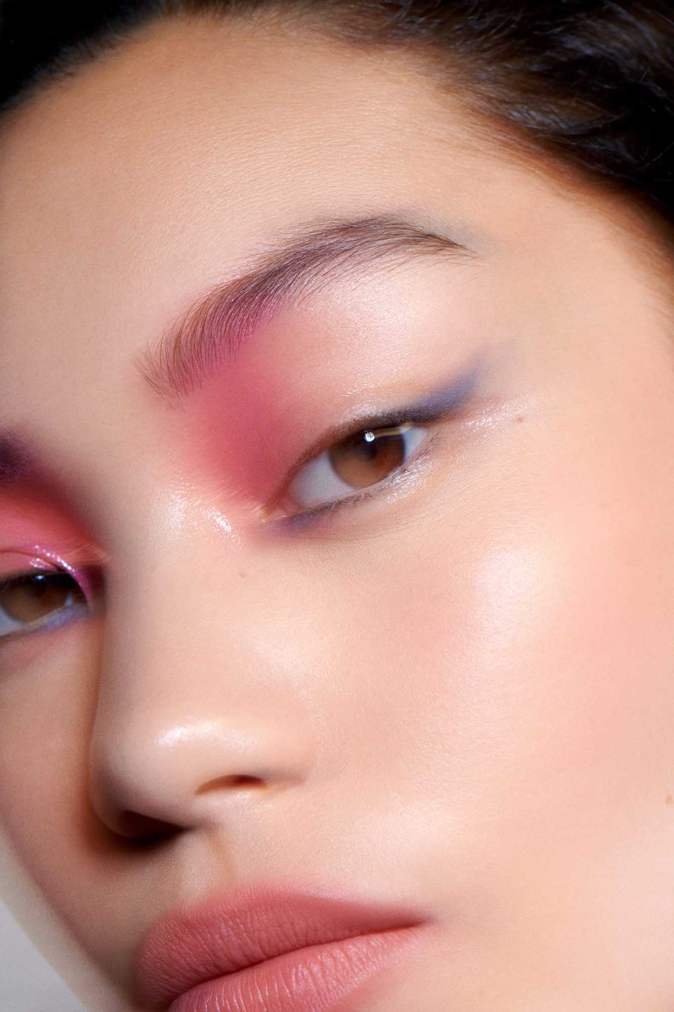 Close-up of a model's face with pink blush-toned eyeshadow, violet liner and glossy skin, retouched beauty shot.