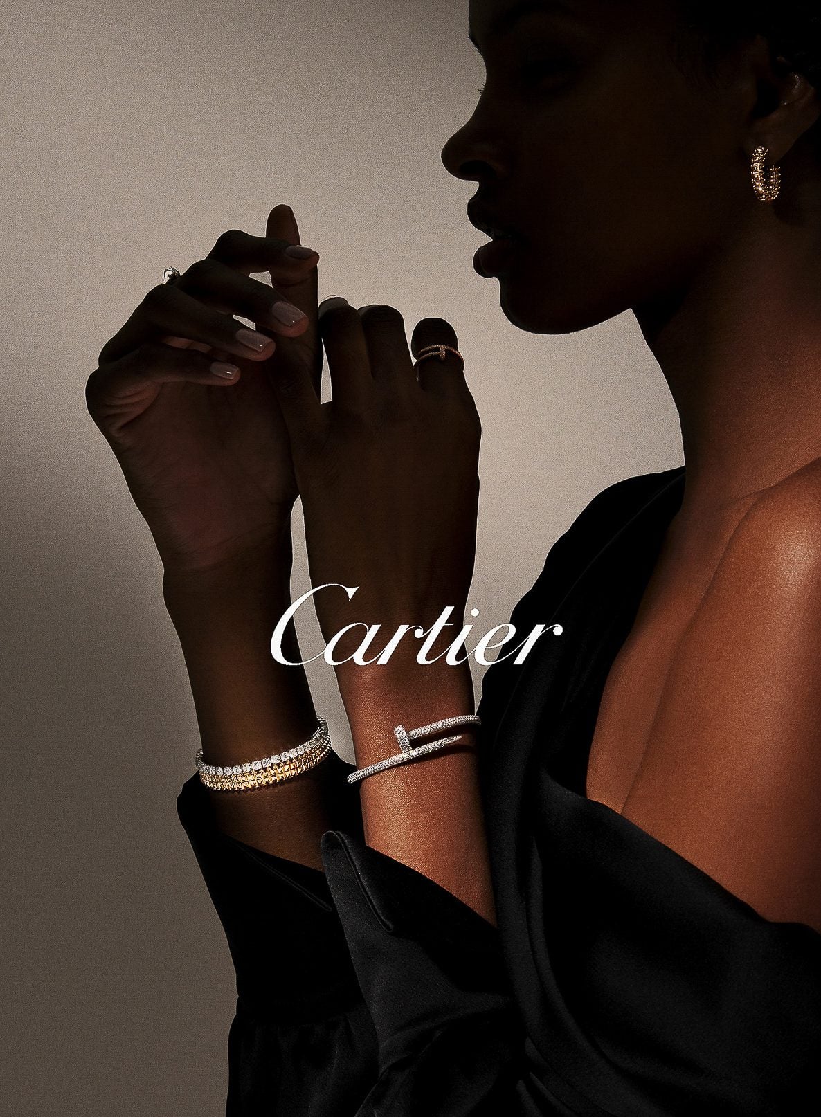 Model in profile wearing a black satin top, diamond bangles, a Juste un Clou bracelet and hoop earrings, for Cartier.