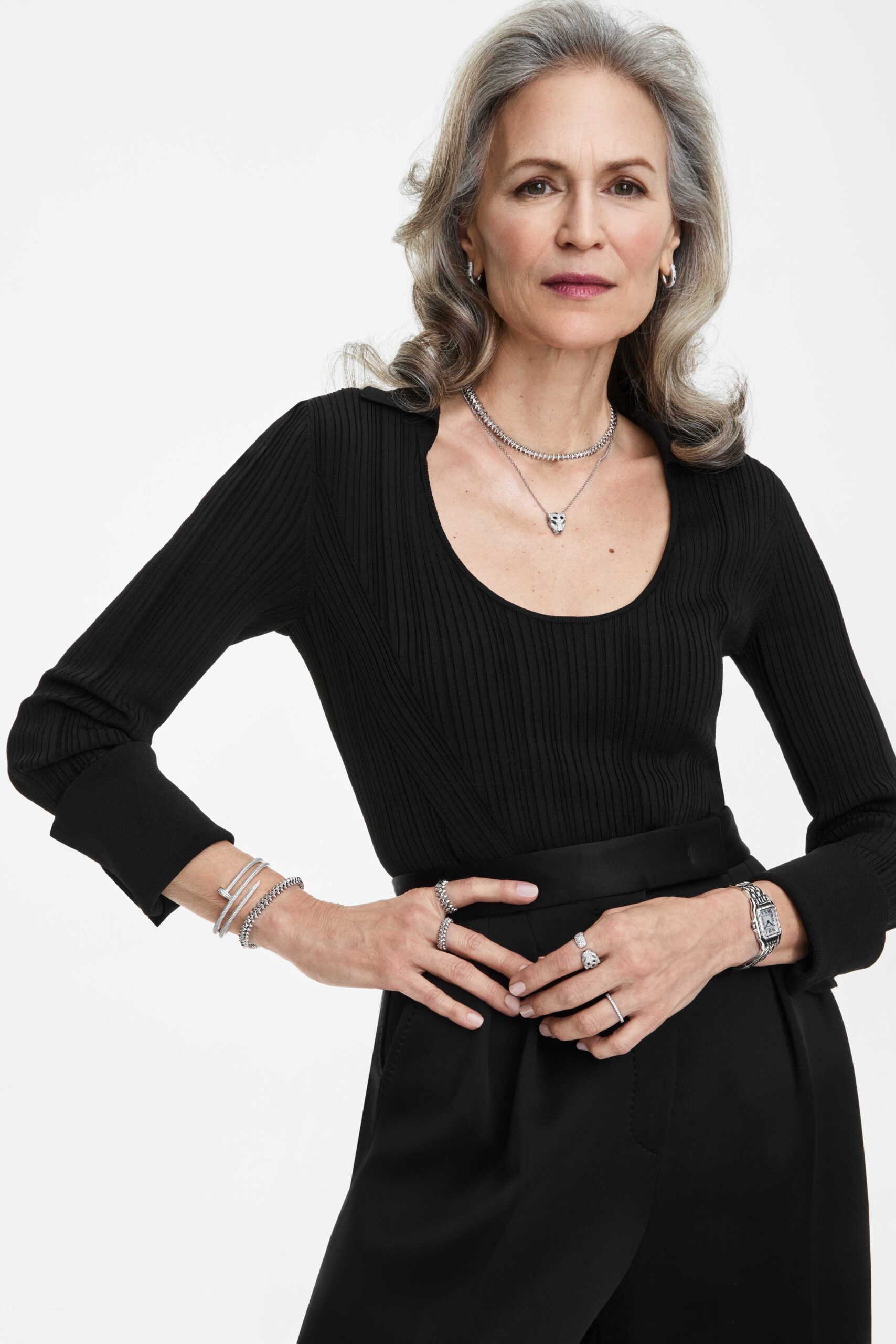 Silver-haired model in a black ribbed top and trousers, wearing silver necklaces, bracelets, rings and a watch, for Cartier.