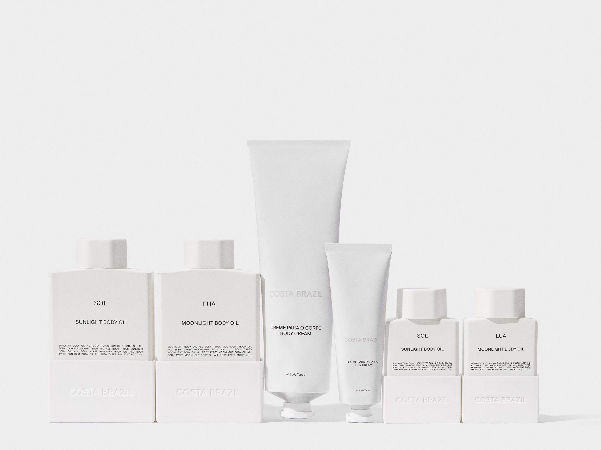 Still life of white Sol and Lua body oil bottles and body cream tubes lined up on a pale grey backdrop, for Costa Brazil.