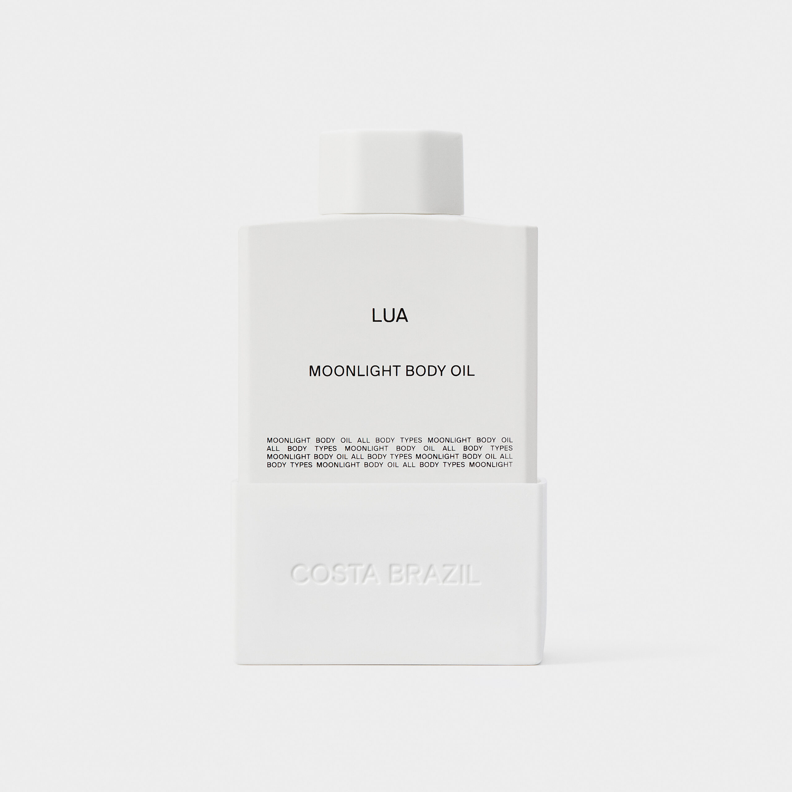 White Lua Moonlight Body Oil bottle with embossed sleeve, a still life on a pale grey backdrop, for Costa Brazil.
