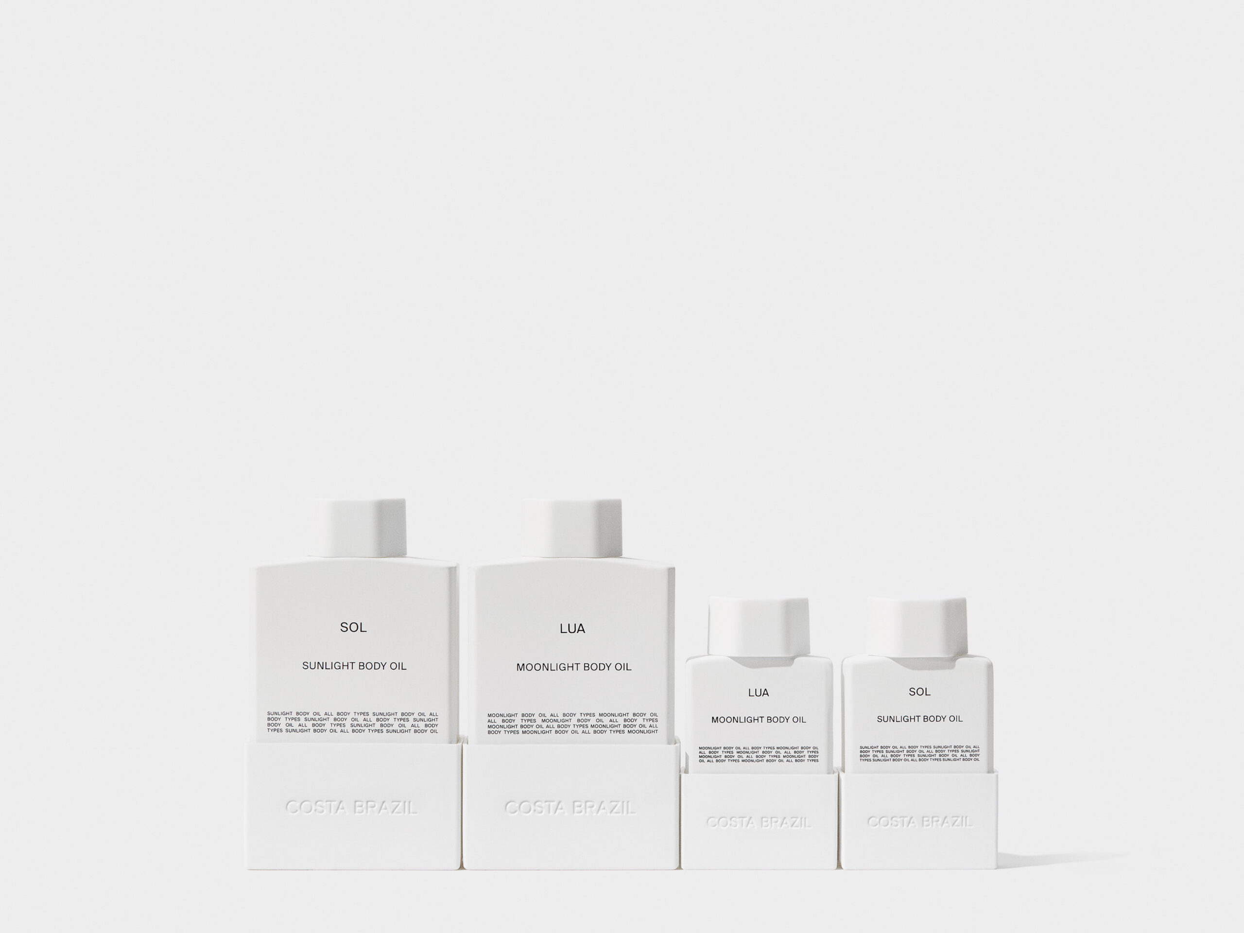 Four white bottles of Sol sunlight and Lua moonlight body oil in two sizes on a white background, for Costa Brazil.