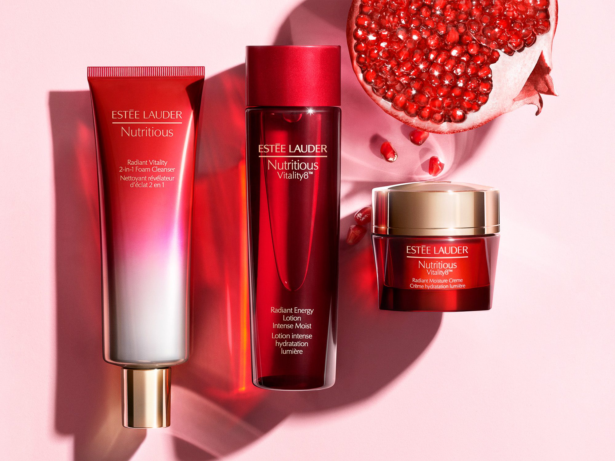 Red Nutritious cleanser, lotion and moisture creme beside a halved pomegranate on pink, for Estée Lauder.