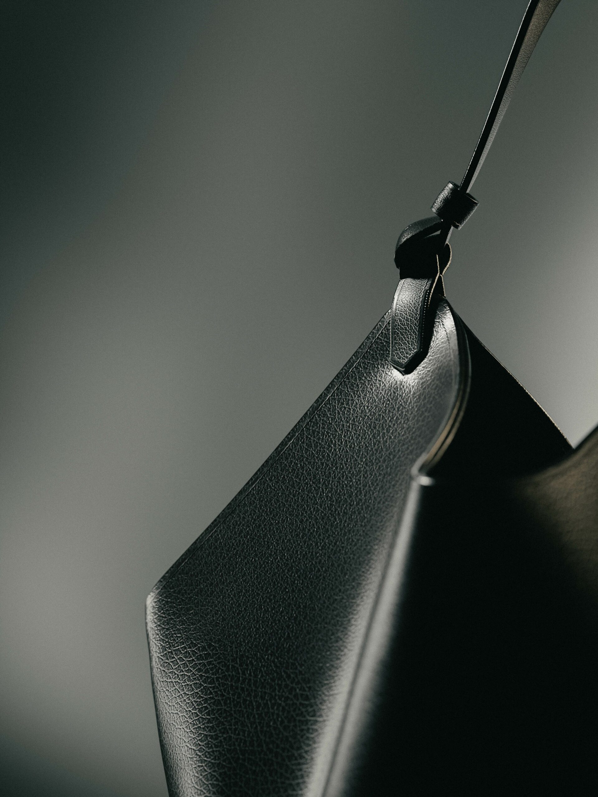 Close-up of a black pebbled leather bag with a knotted strap against a grey gradient, still life, for Khaite.