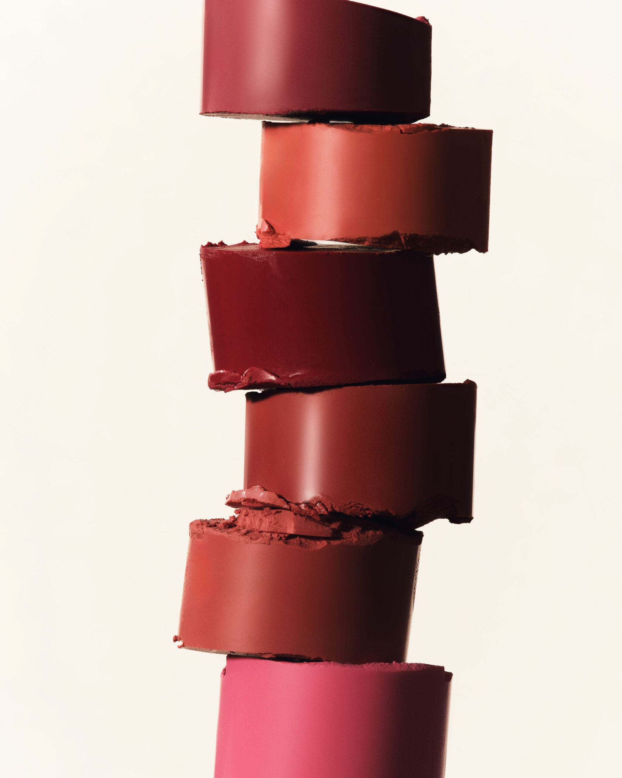 Stack of cut lipstick bullets in red, coral, berry and pink shades on a cream background, for Kylie Cosmetics.