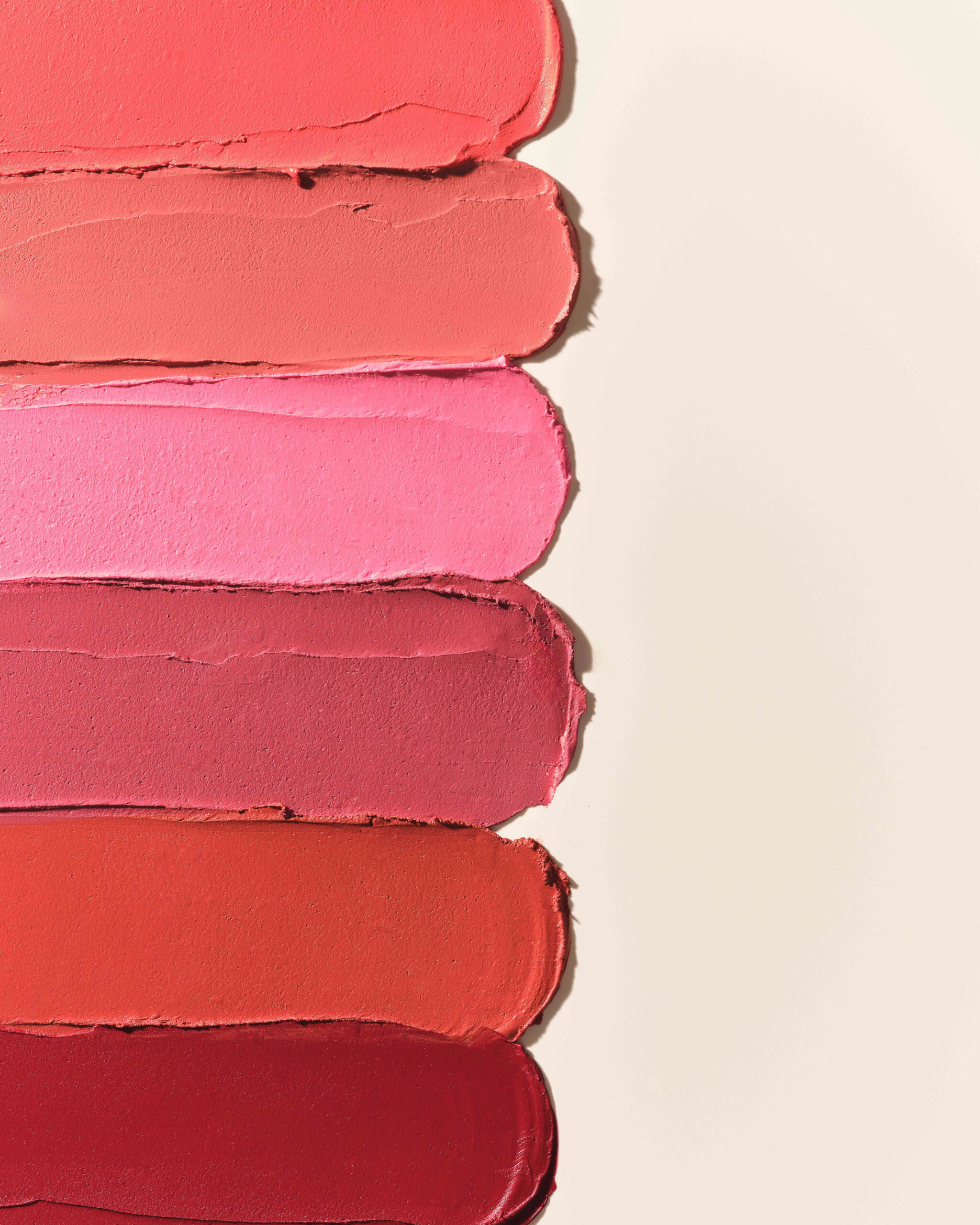 Six lipstick swatches in coral, pink, rose, orange and red smeared across a cream background, for Kylie Cosmetics.
