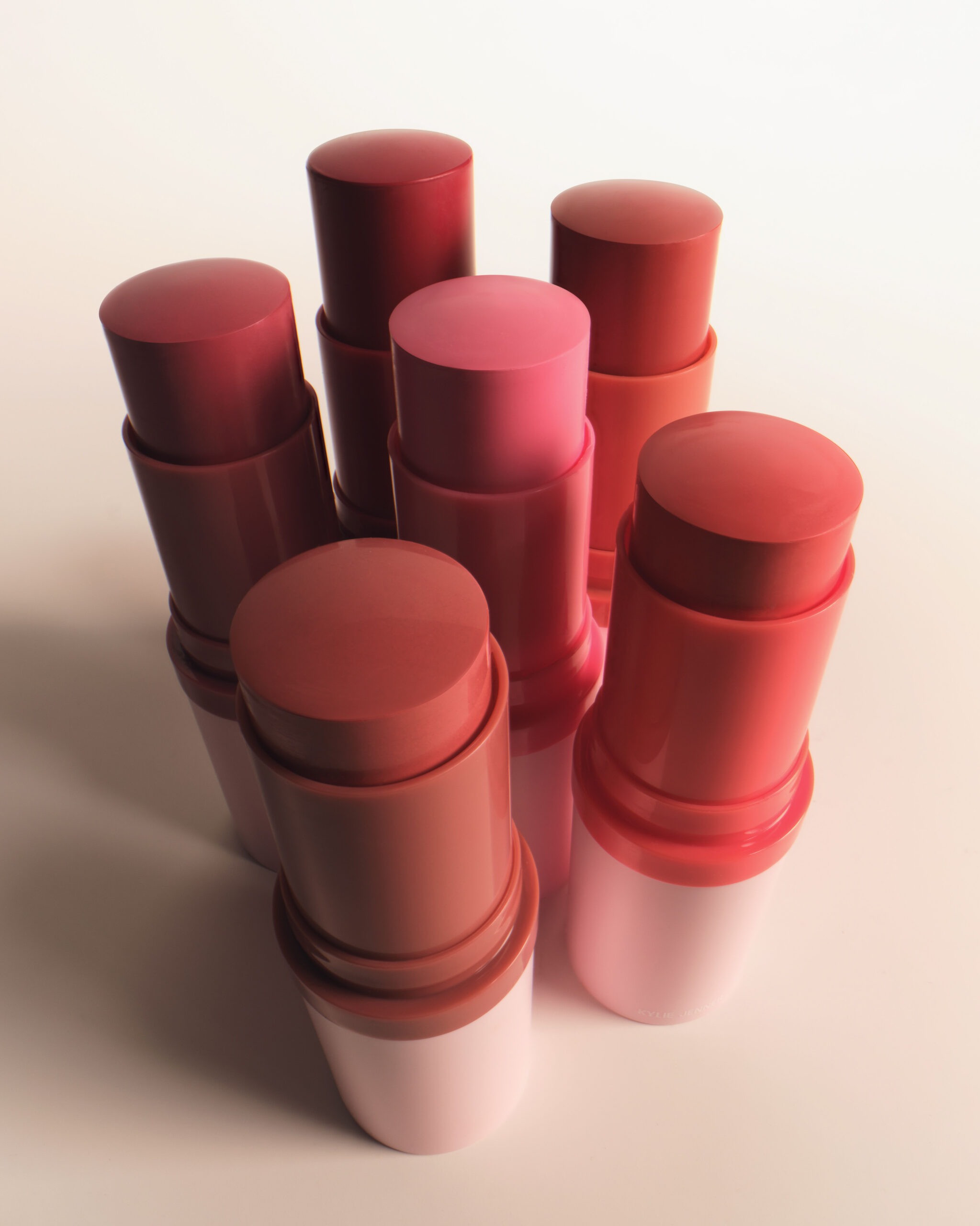 Six blush sticks in shades of pink, coral and red with uncapped tips, standing on a pale backdrop, for Kylie Cosmetics.