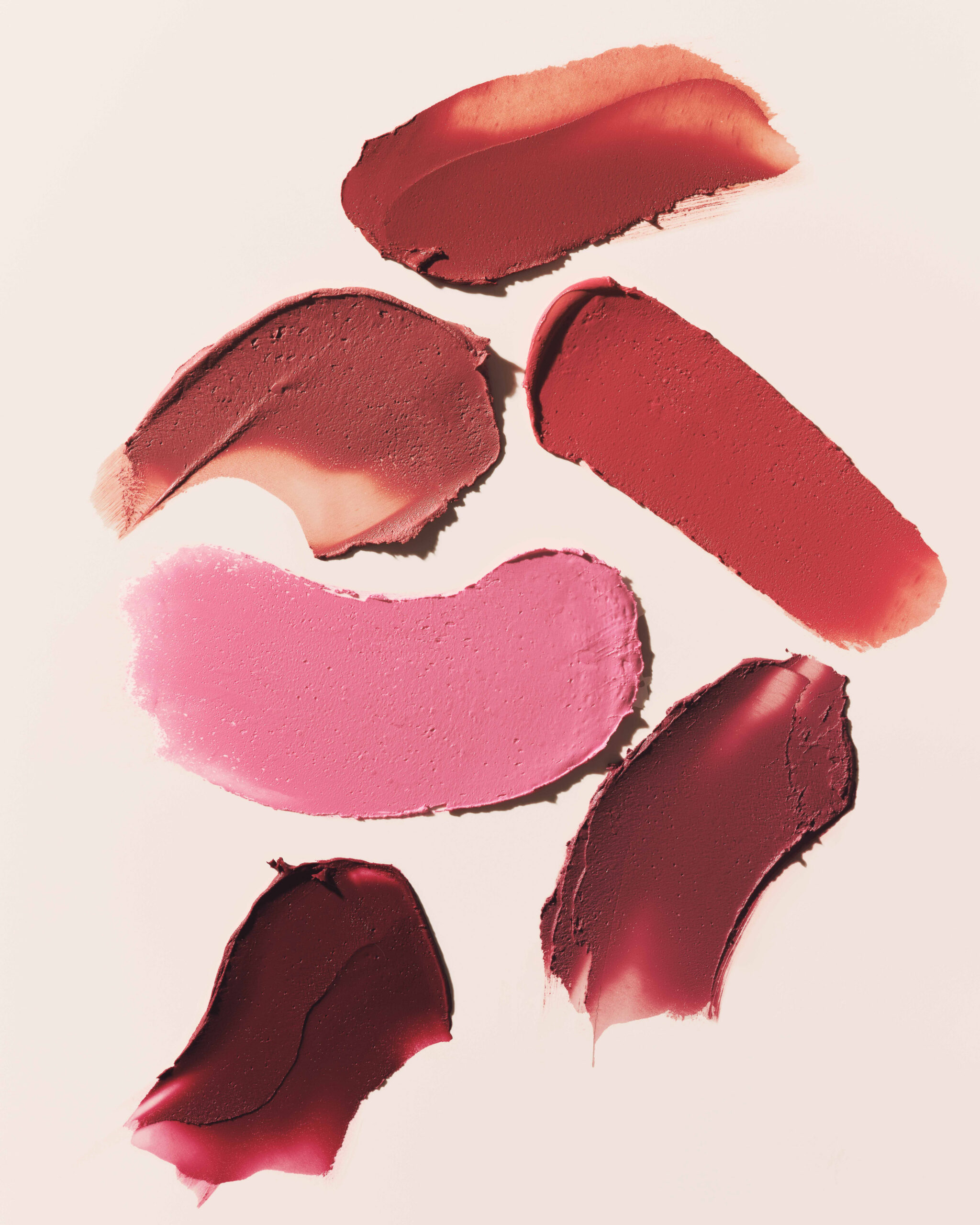 Six lipstick swatches in pink, rose, red and deep berry smeared across a pale blush background, for Kylie Cosmetics.