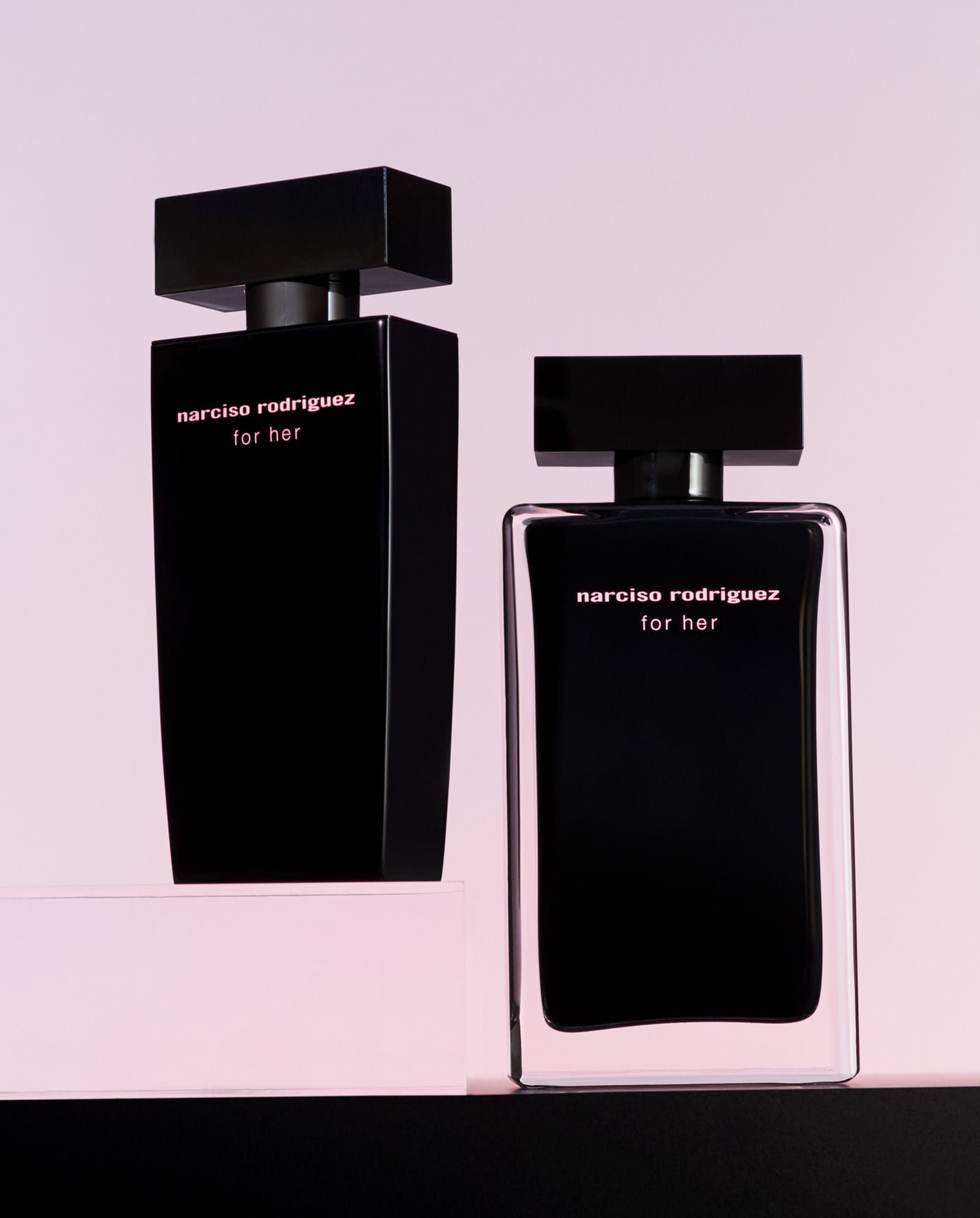 Two black For Her fragrance bottles on pink and black plinths against a soft pink backdrop, for Narciso Rodriguez.
